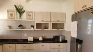 Eine moderne Küche mit hellen Holzschränken, einer schwarzen Arbeitsplatte, einem Edelstahlkühlschrank und einer Mikrowelle.