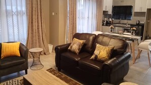 Ein modernes Wohnzimmer mit einer schwarzen Ledersofa, einem kleinen runden Couchtisch und einem Essbereich mit weißem Tisch und Stühlen.