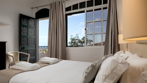 Ein Hotelzimmer mit Bett, Stuhl, einem Fenster mit Vorhängen und Blick nach draußen.