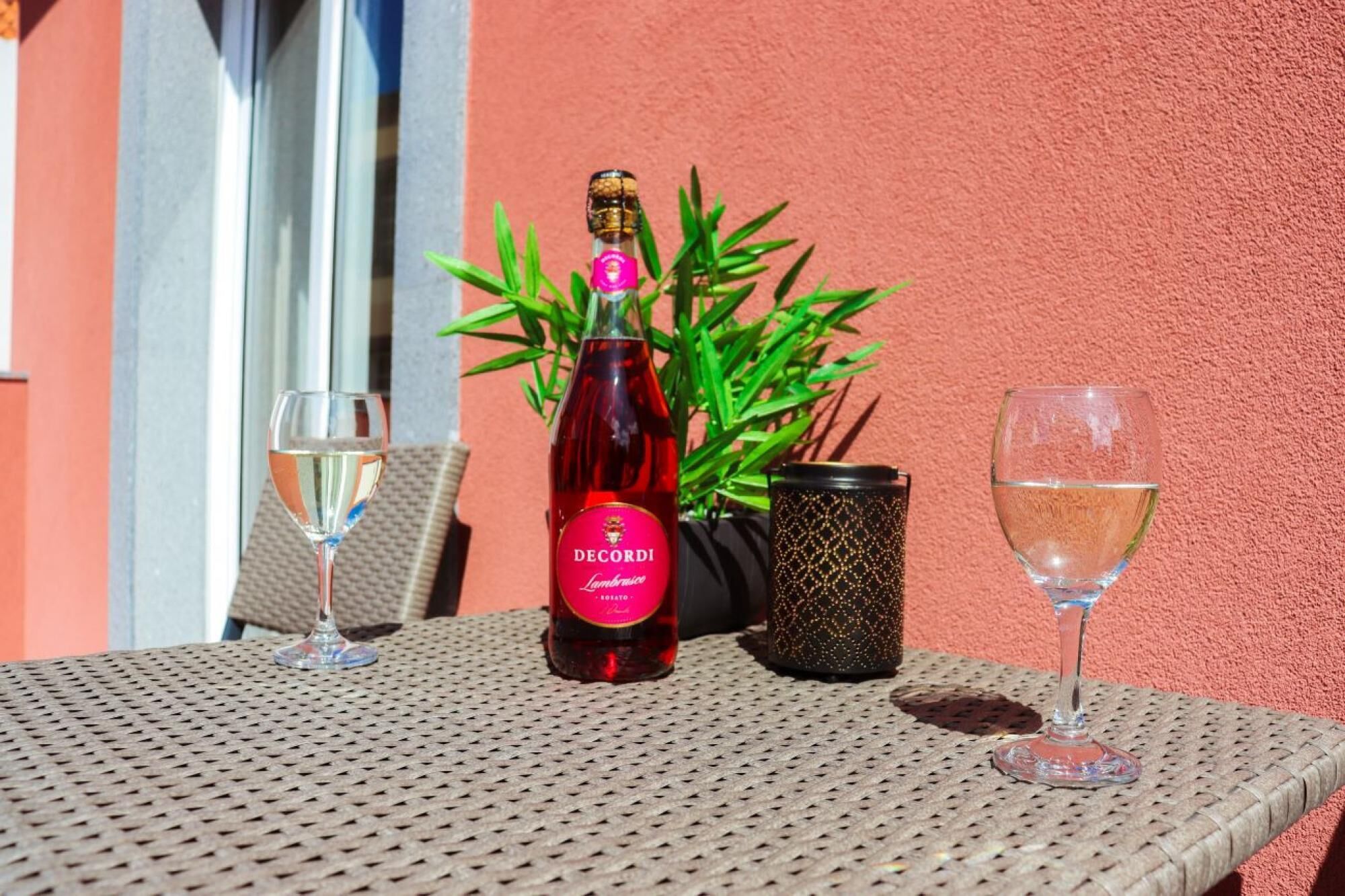 A table with a bottle of De Cordi wine, two glasses, and a decorative plant.