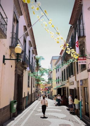 A narrow street lined with buildings, decorated with hanging yellow and green flowers.