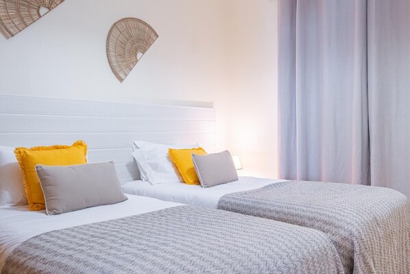 A hotel room with two beds, white bedding, and decorative wall fans. - My Place in Funchal by Homie (Funchal)