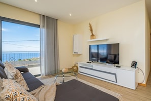 Relax in a spacious living area with a large flat-screen TV, comfortable seating, and a balcony with an outside view.