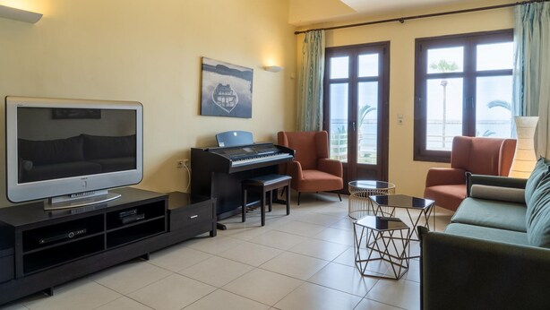 Ein Wohnzimmer mit Flachbildfernseher, einem Klavier, zwei Sesseln, einer Couch und einem Tisch.