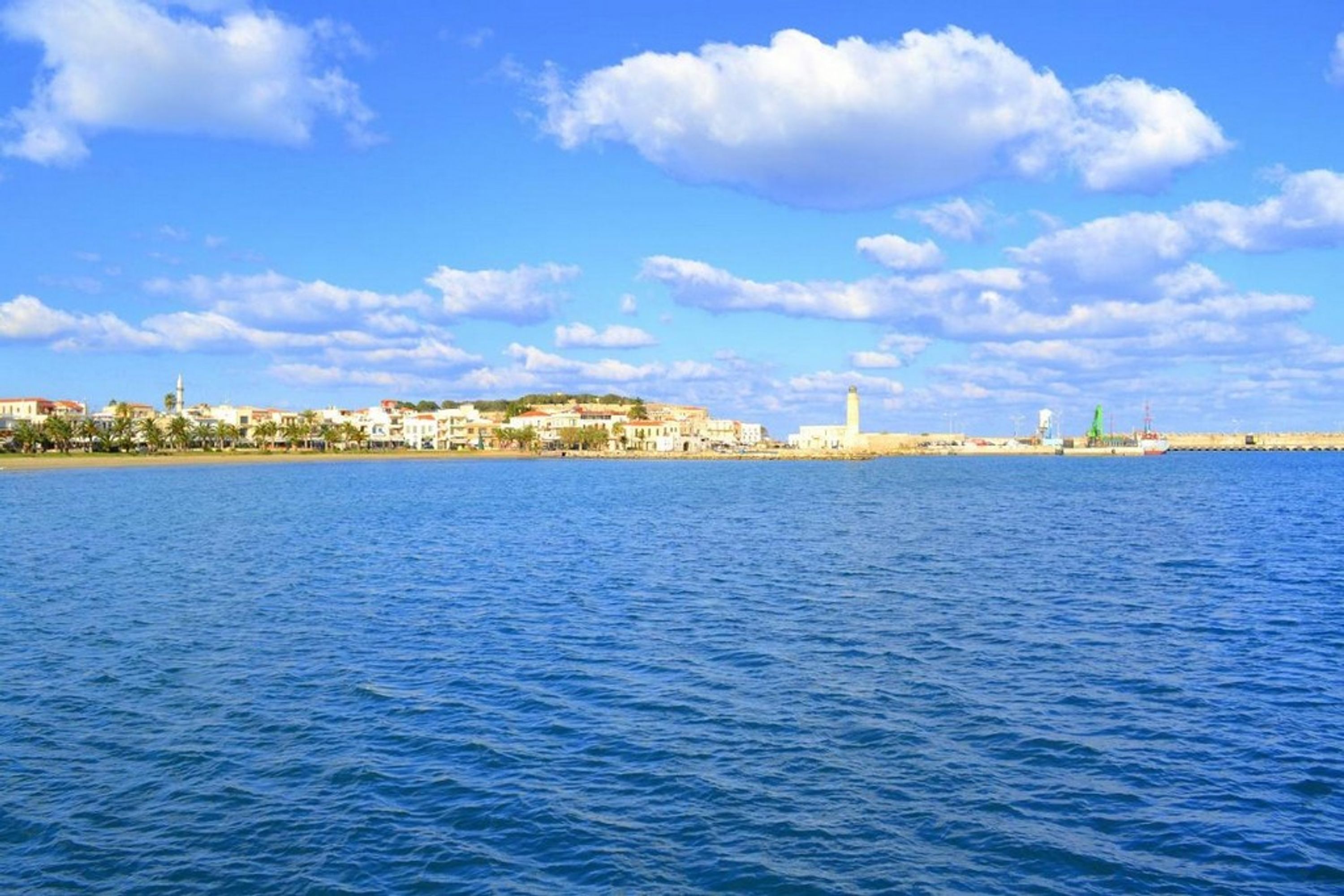 Un paisaje urbano costero con edificios a lo largo de la costa, una torre destacada y un cielo azul despejado.
