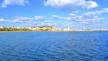 Un paisaje urbano costero con edificios a lo largo de la costa, una torre destacada y un cielo azul despejado.