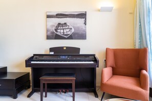 Um piano com um banquinho, uma cadeira e um quadro de um barco na água.