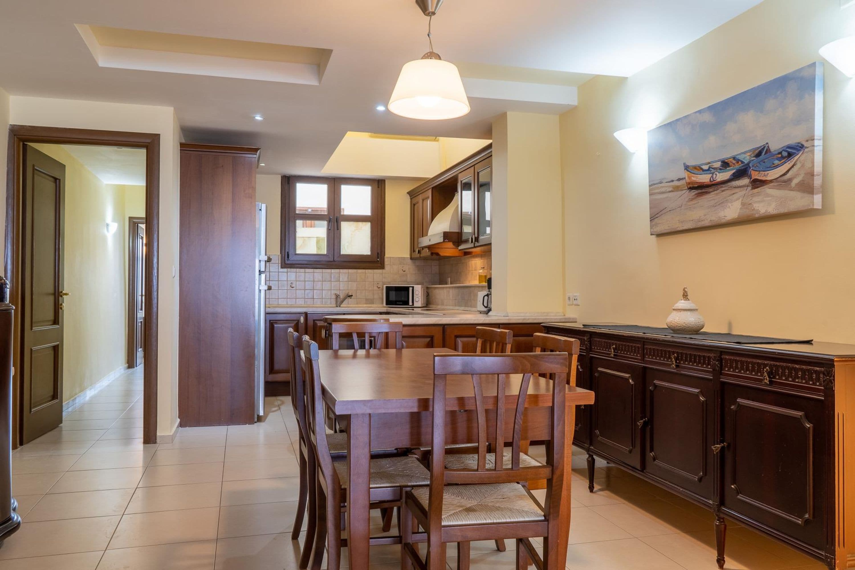 Una cocina amplia con armarios de madera, una mesa de comedor con sillas y un cuadro con barcos en la pared.