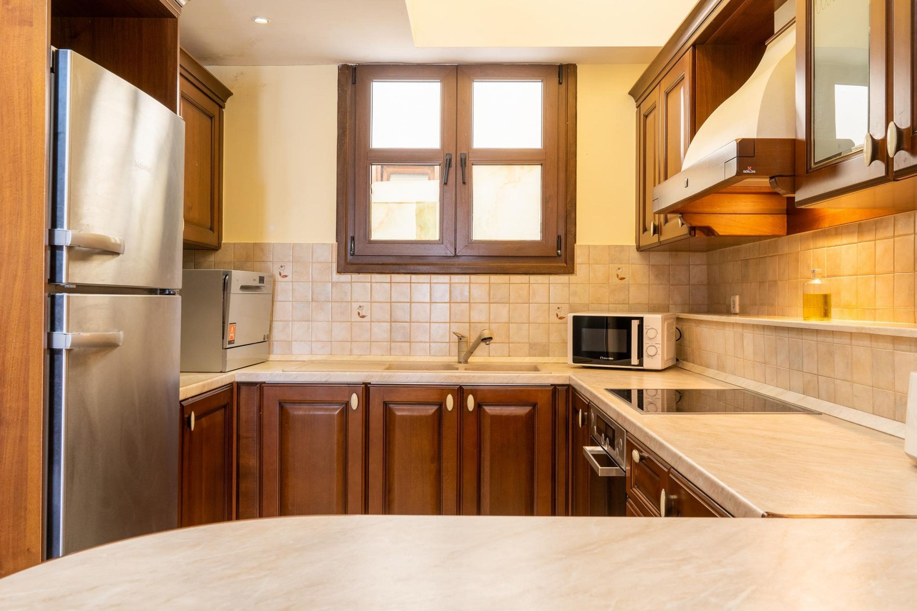 Una cocina con armarios de madera, un refrigerador de acero inoxidable, un microondas y una ventana sobre el fregadero.