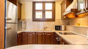 Una cocina con armarios de madera, un refrigerador de acero inoxidable, un microondas y una ventana sobre el fregadero.
