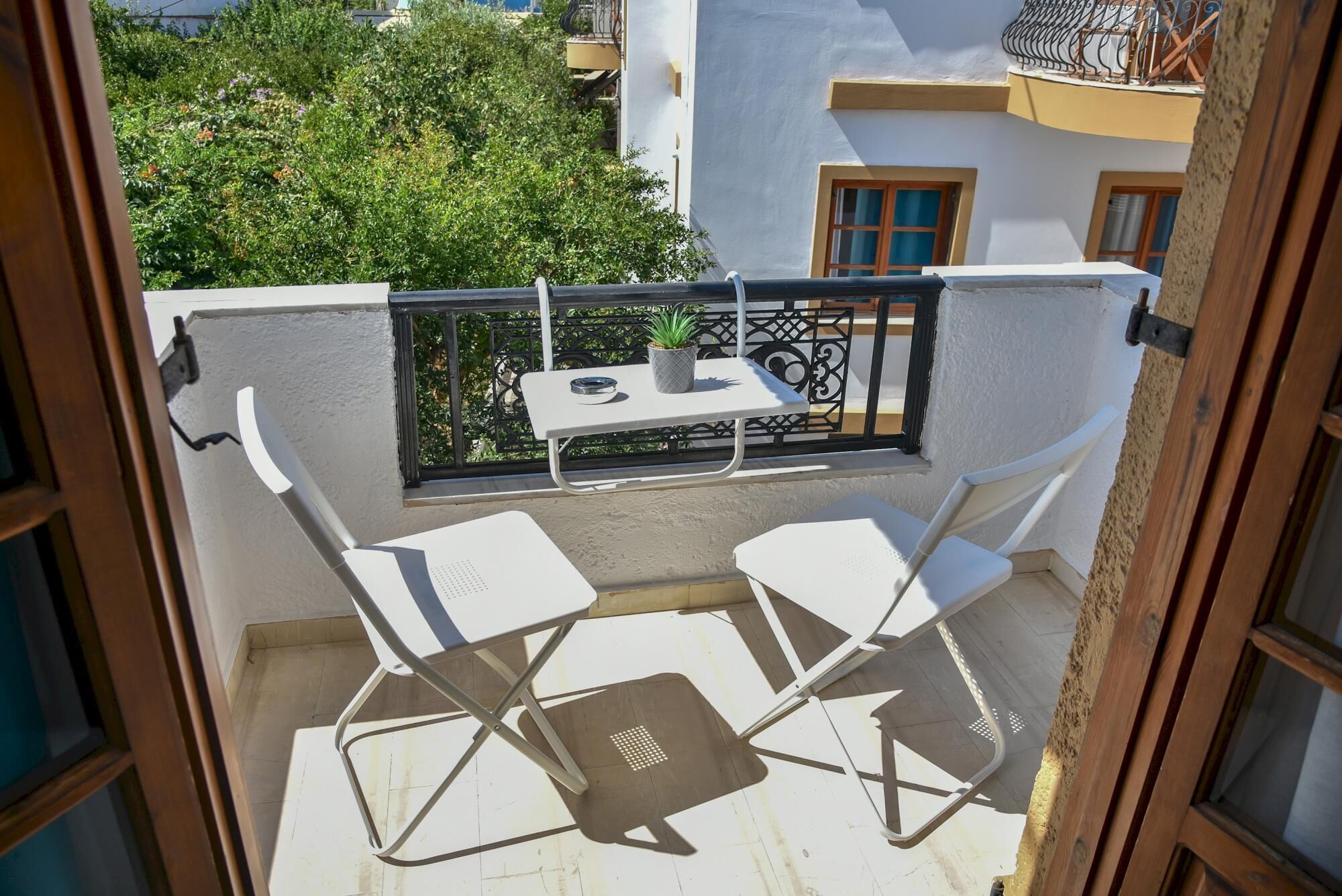 Un balcon avec deux chaises blanches et une petite table, entouré d’une rambarde en métal noir.