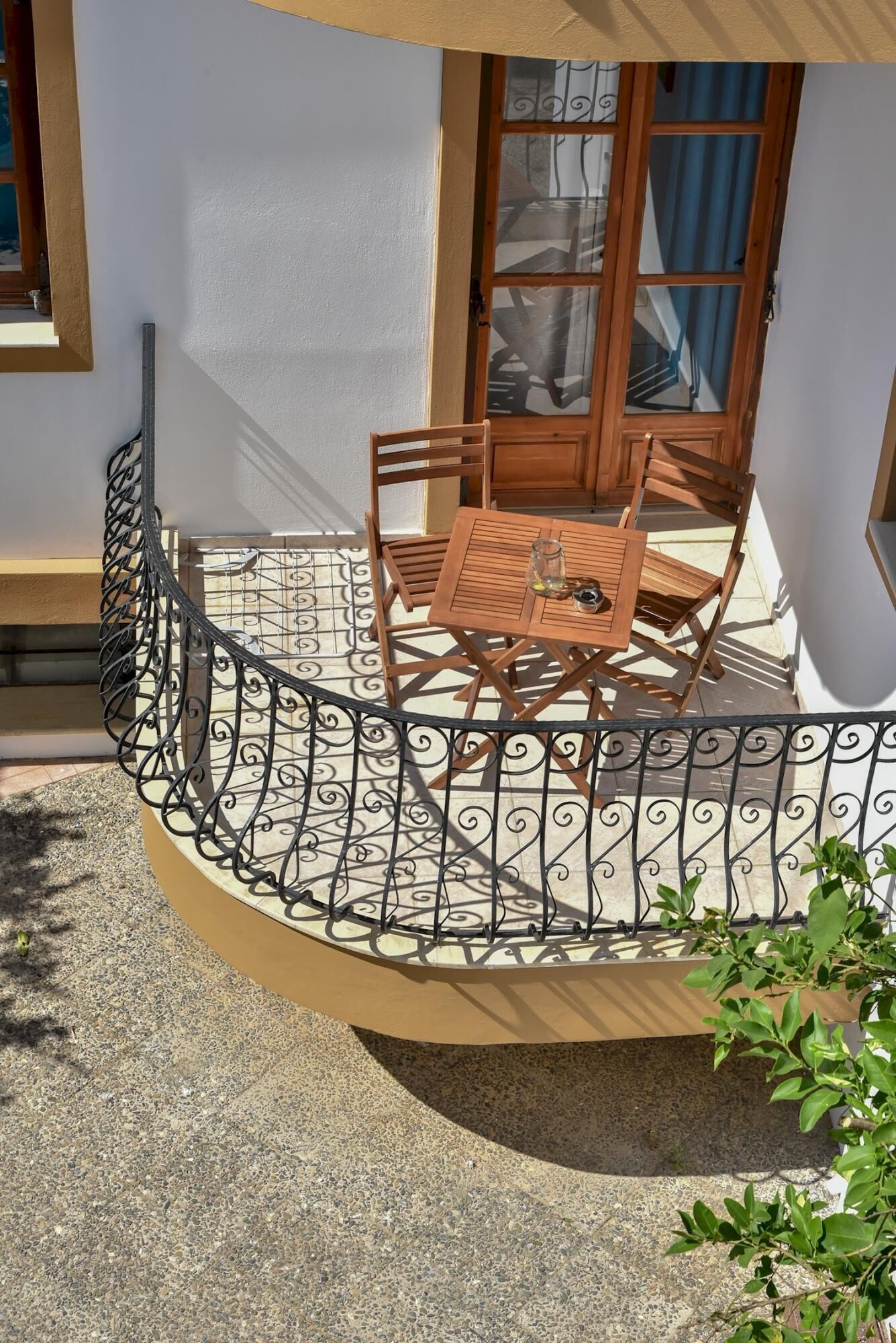 Un pequeño patio al aire libre con una mesa redonda y dos sillas, rodeado por una valla metálica decorativa.