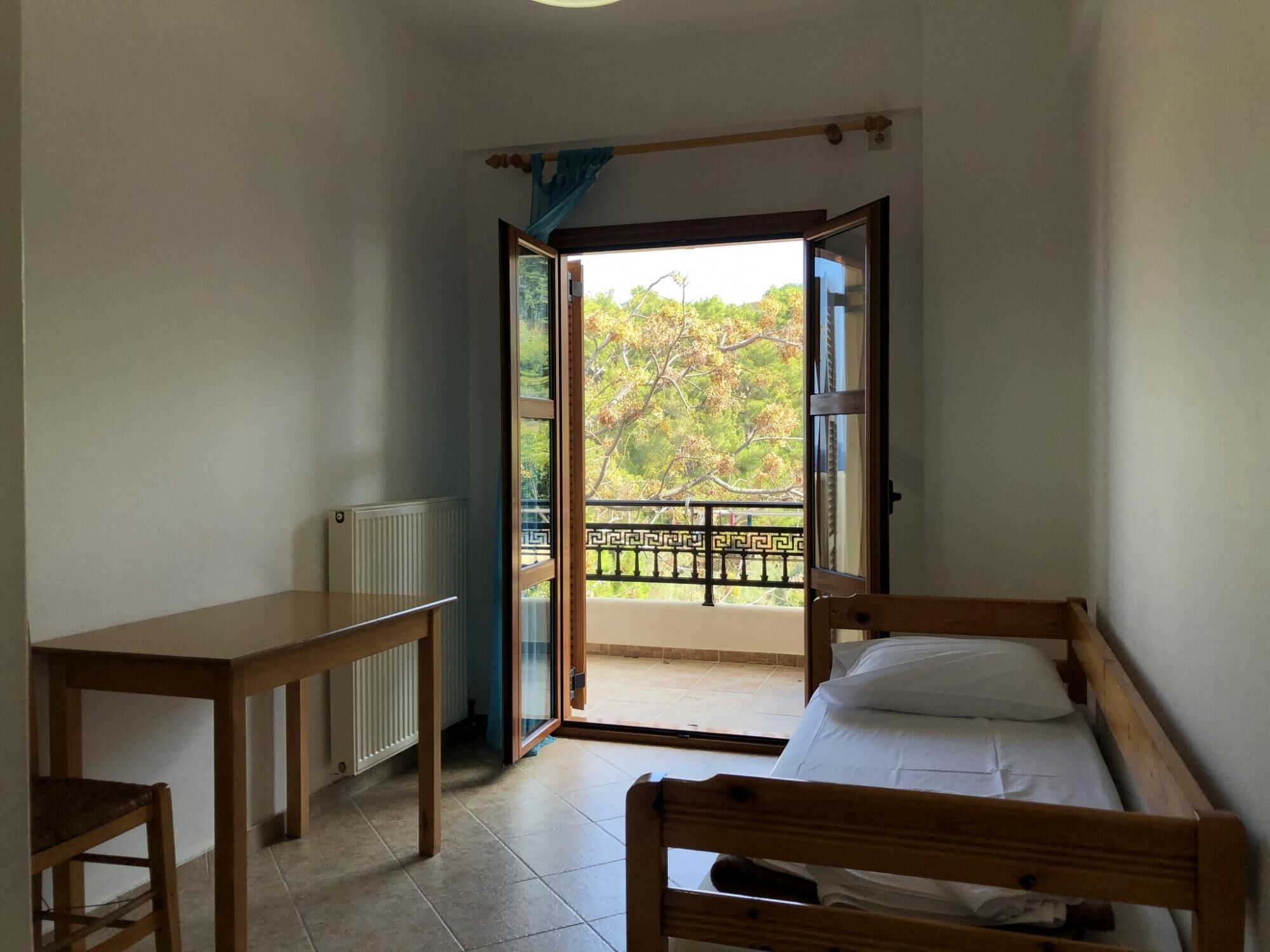 A bedroom with a bed, a table, and a view of a balcony with a railing.