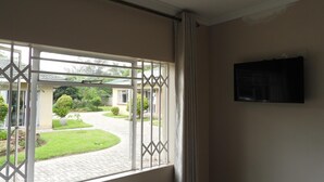 Een kamer met een raam dat uitkijkt over een tuin en een gebouw.