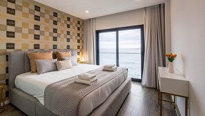 Una habitación de hotel moderna con una cama grande, vista al mar y un escritorio con un florero.