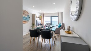 Una sala de estar moderna con comedor, ventanas amplias y vista al mar.