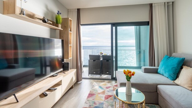 Una sala de estar moderna con un televisor de pantalla plana grande, un sofá, una mesa de centro y un balcón con vista al mar.