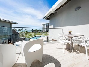 Un balcon avec vue sur la piscine, des chaises blanches et une table.