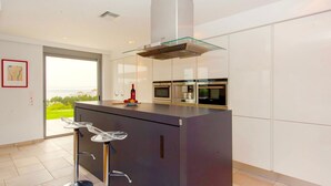A modern kitchen with a glass-top island, stainless steel appliances, and a view of greenery outside. - Luxury Villa Stella With Private Swimming Pool (Chania)