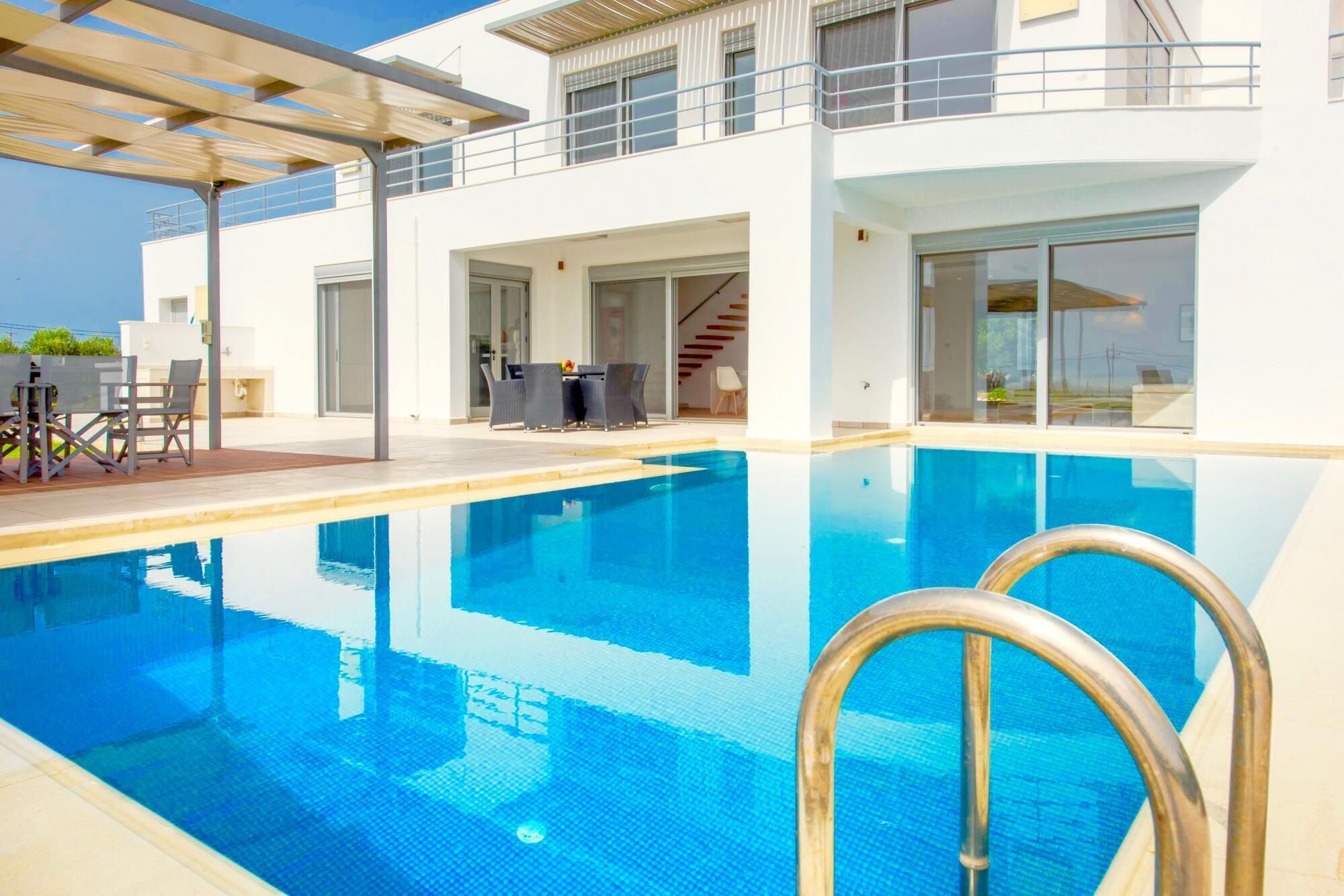 A modern pool area with clear blue water, a covered seating area, and a staircase leading to an upper level.