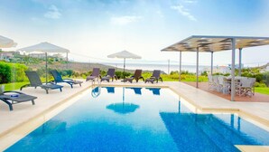 A swimming pool with lounge chairs and umbrellas, surrounded by greenery and overlooking a coastal landscape. - Luxury Villa Stella With Private Swimming Pool (Chania)