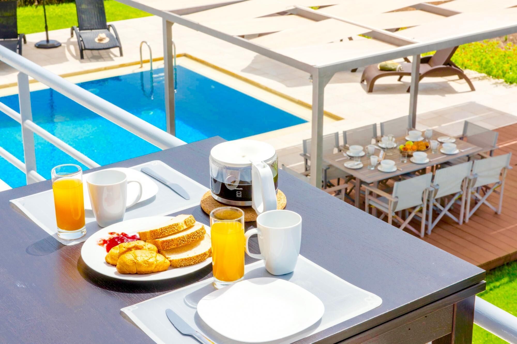 A breakfast setup with toast, juice, and coffee on an outdoor table near a swimming pool.
