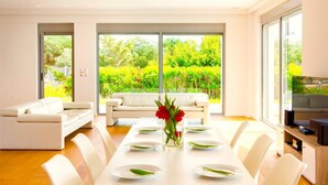 A modern dining room with a white table set for six, a sofa, and a TV on a wooden cabinet. - Luxury Villa Stella With Private Swimming Pool (Chania)