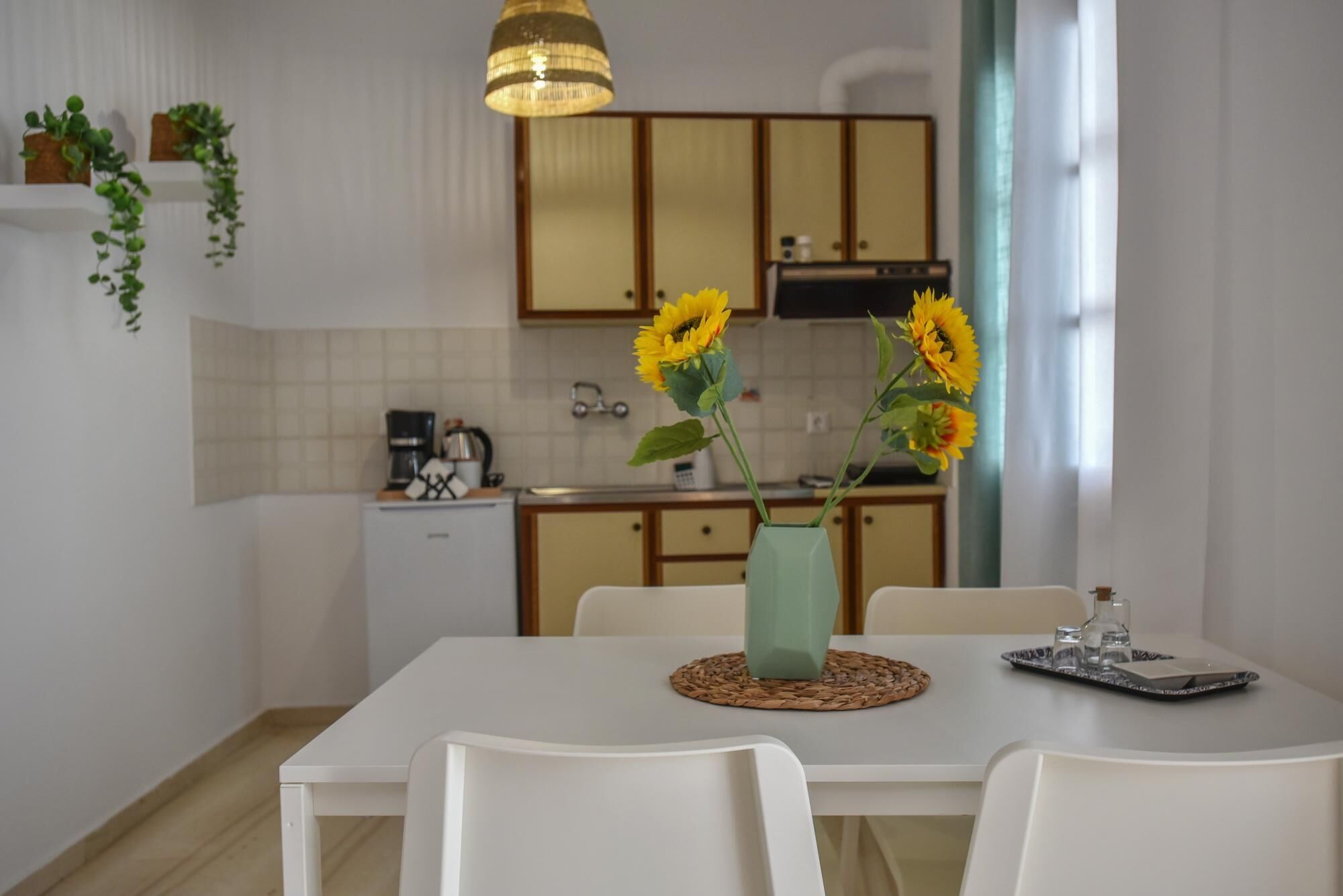 Een moderne keuken met witte kasten, een koffieapparaat en een eettafel met stoelen. Er staan zonnebloemen op tafel.