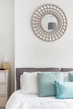 Cozy retreat with a round mirror, grey headboard, and plush bedding.