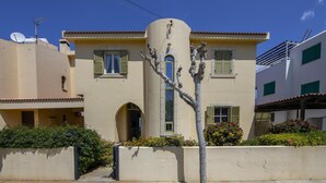 A two-story building with a beige facade, green shutters, and a central arched doorway. - Sirina Waterfront House (Paralimni)