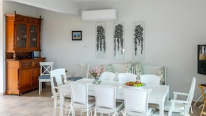 A dining area with a white table, white chairs, and a wooden cabinet. - Sirina Waterfront House (Paralimni)