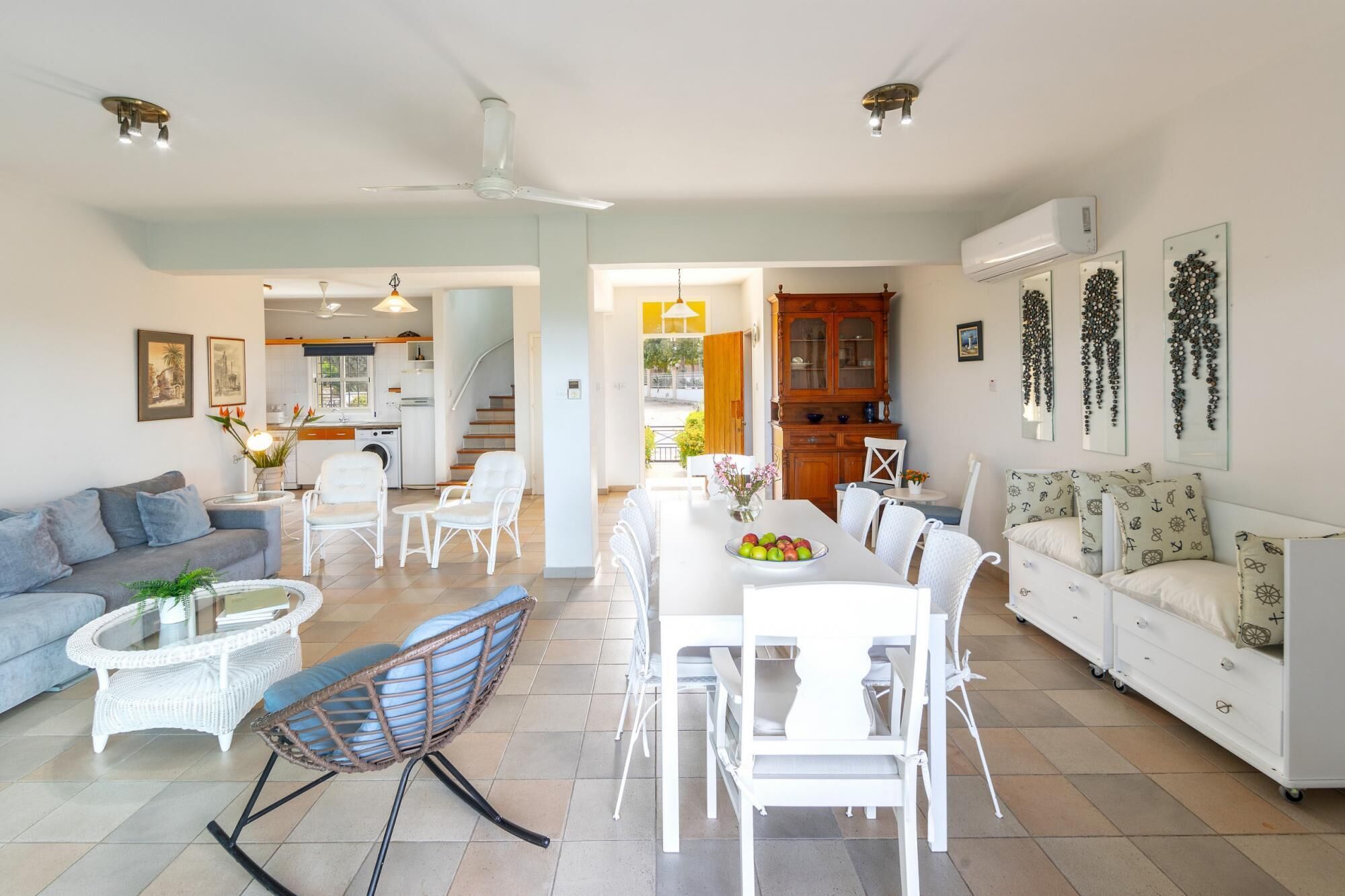 A spacious living area with a sofa, chairs, a dining table with fruit, and a kitchen in the background.