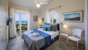 A bedroom with a bed, a chair, a desk, a TV, and a window with a view. - Sirina Waterfront House (Paralimni)