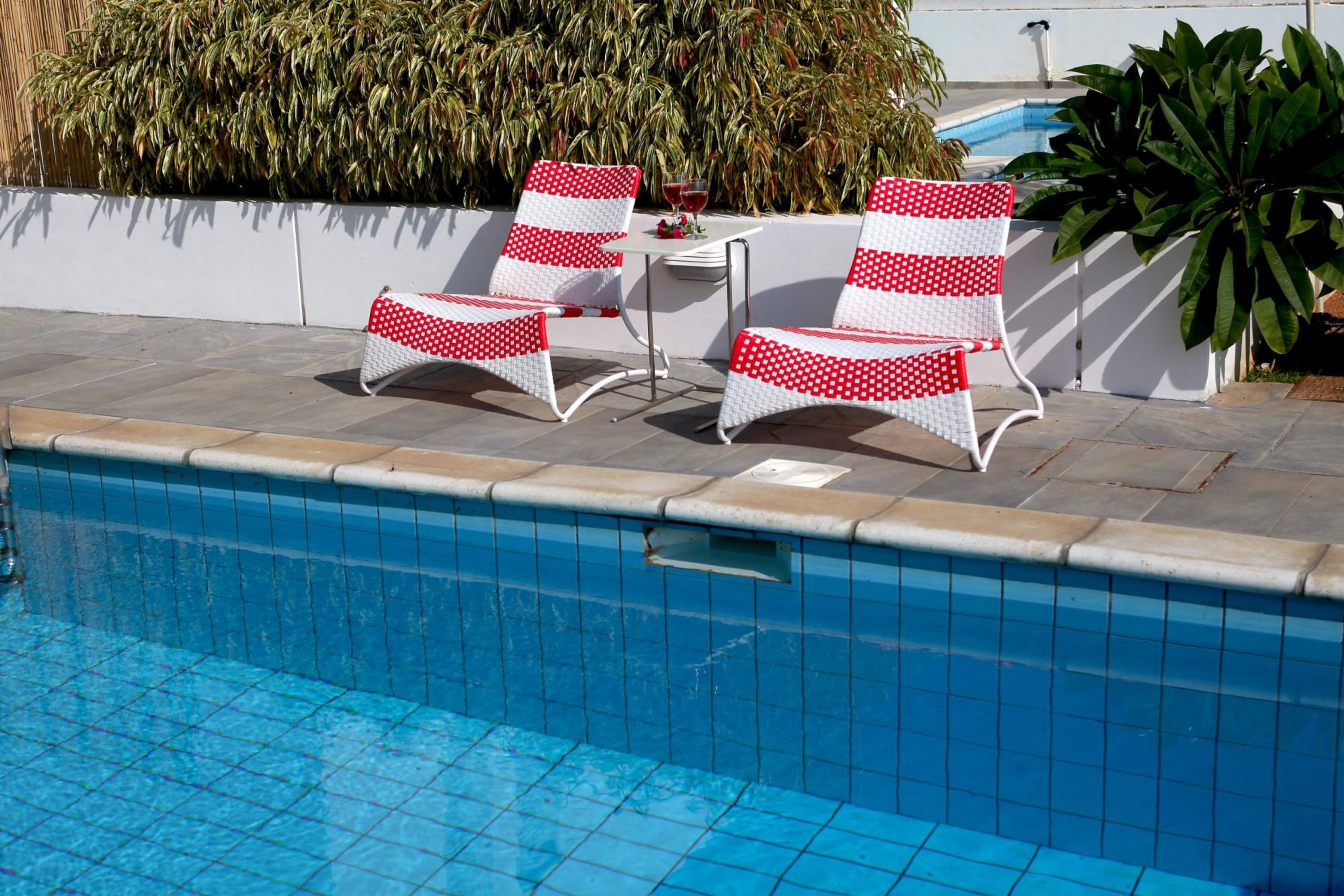 A poolside area with a tiled pool, two white chairs with red polka dots, and a small table with a glass of red wine.