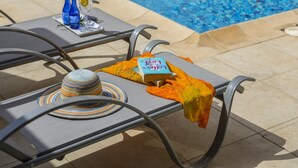Un espace aménagé au bord de la piscine, avec des chaises longues, un livre et un chapeau.