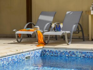 Un área junto a la piscina con sillones de descanso y una piscina con baldosas.