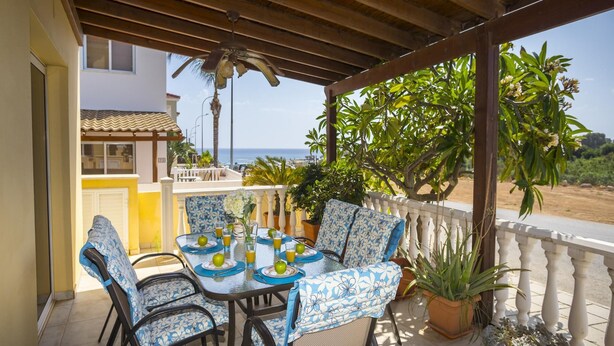 Un espace extérieur abrité, aménagé pour les repas, avec une table pour deux, entourée de chaises dont les coussins sont ornés de motifs floraux bleus et blancs.