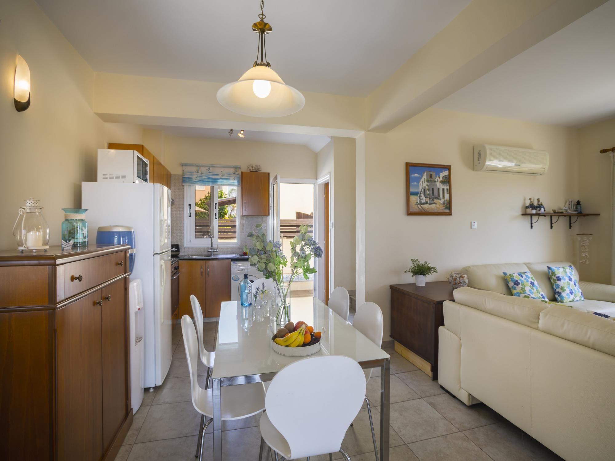 A modern kitchen with white cabinets, a dining table with chairs, and a beige sofa in the living area.