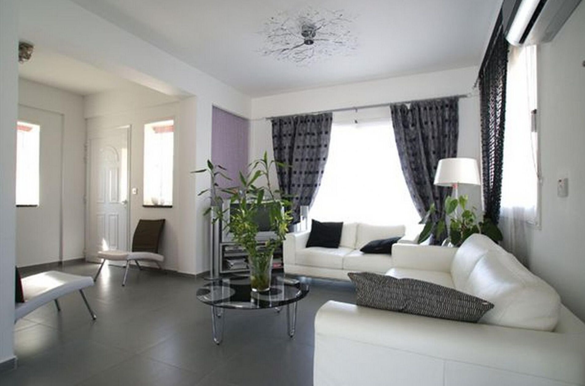 A modern living room with a white sofa, a glass coffee table, and a potted plant.