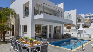 Een modern huis met twee verdiepingen, een zwembad, buiten zitplaatsen en een balkon.