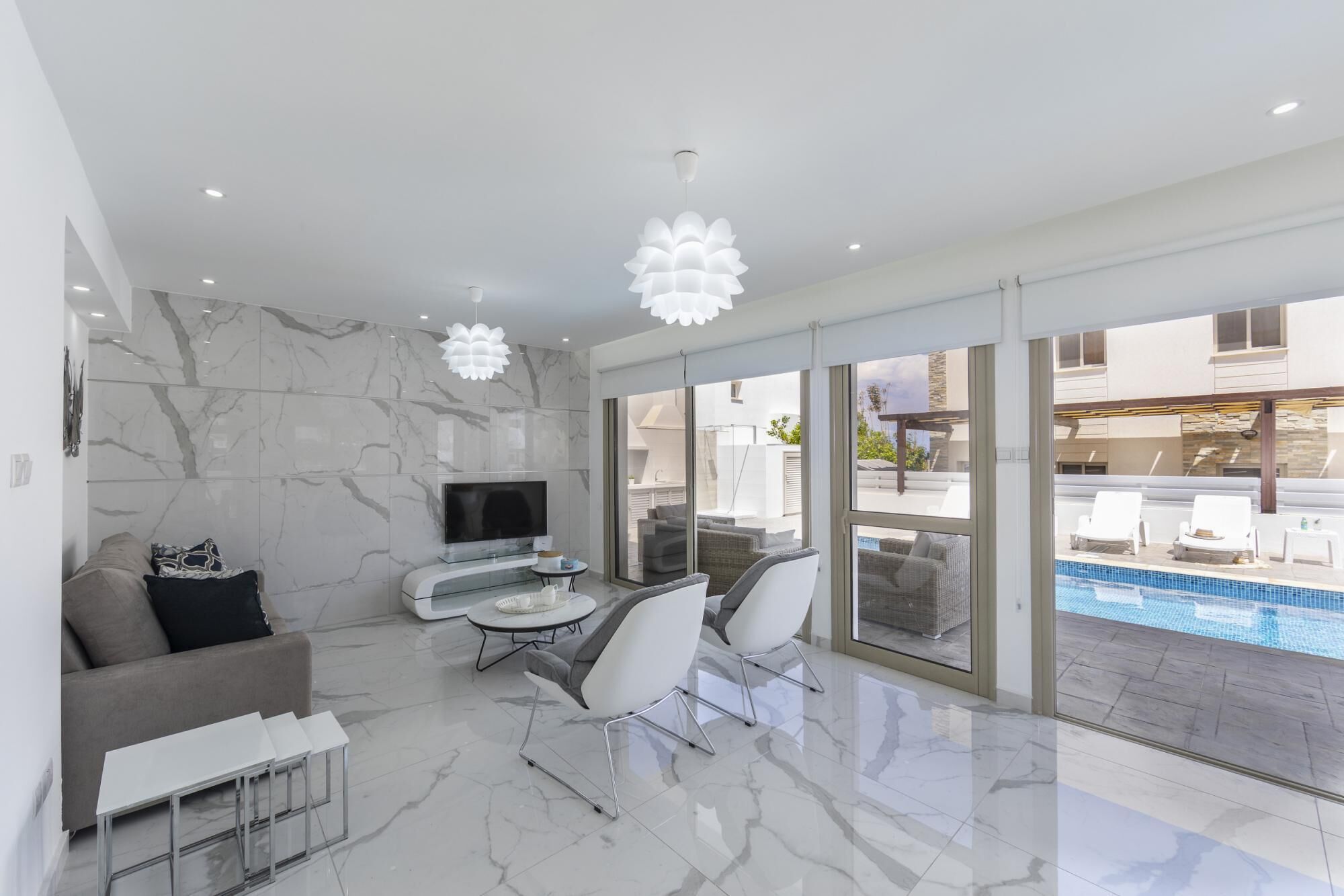 A modern living room with a TV, seating, and a pool view.