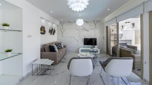 Een moderne woonkamer met een bank, twee fauteuils, een televisie en een glazen salontafel.