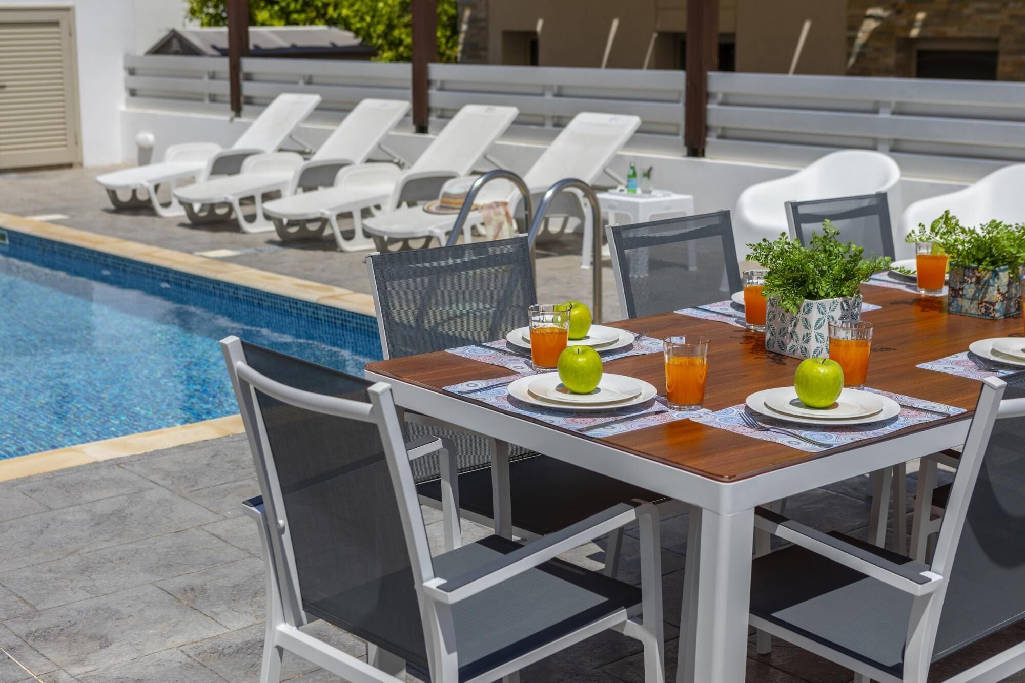 A poolside dining area with a table set for two, surrounded by lounge chairs.