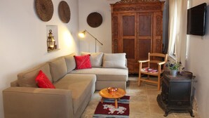 Una sala de estar acogedora con un sofá, un armario de madera, un televisor y una mesita con una lámpara.