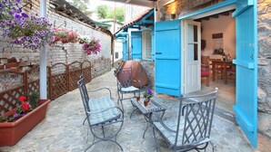 Un patio con suelo de piedra, mobiliario exterior, una parrilla y macetas colgantes de flores.