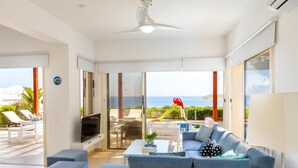A modern living room with a grey sofa, a flat-screen TV, and a ceiling fan. - Protaras Artisan Seafront Villa 6 (Paralimni)