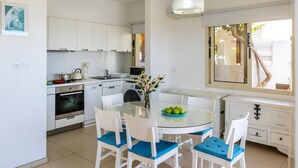 A modern kitchen with white cabinets, a round glass table, and blue cushioned chairs. - Protaras Artisan Seafront Villa 6 (Paralimni)