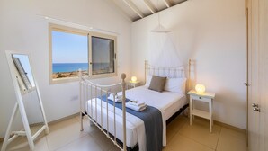 A bedroom with a bed, bedside tables, a window with a view of the beach, and a door. - Protaras Artisan Seafront Villa 6 (Paralimni)