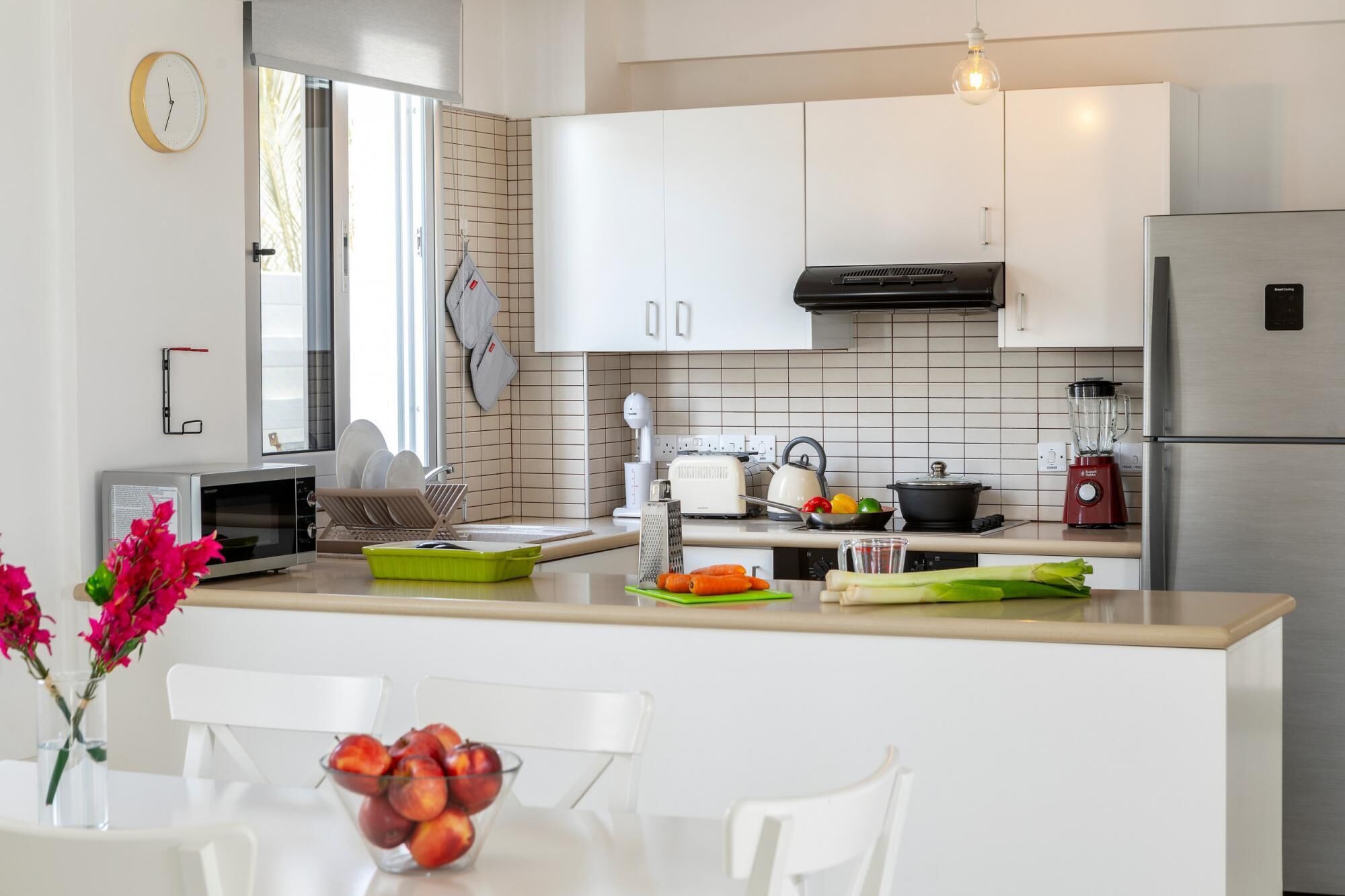 A modern kitchen with white cabinets, a stainless steel refrigerator, a kettle, and a blender on the counter.