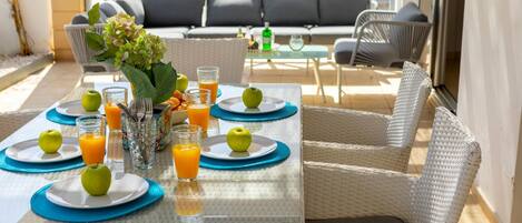 A dining table set with plates, glasses, and apples, surrounded by wicker chairs.
